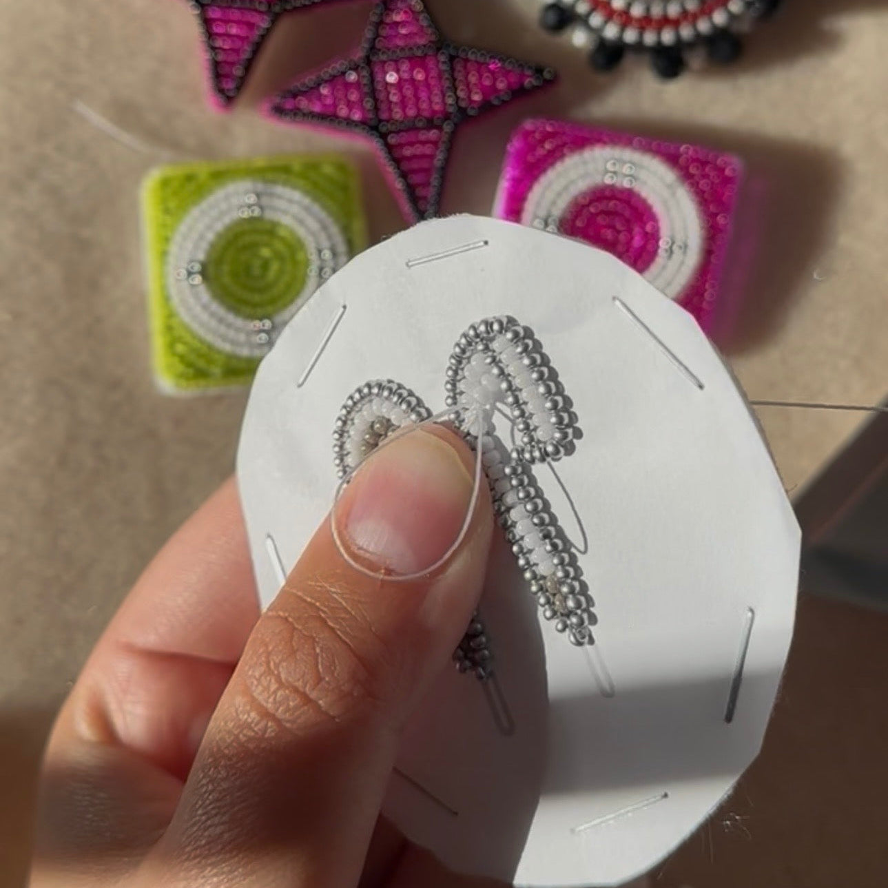 Hand holding a white card with beaded earrings, with more earrings in the background.
